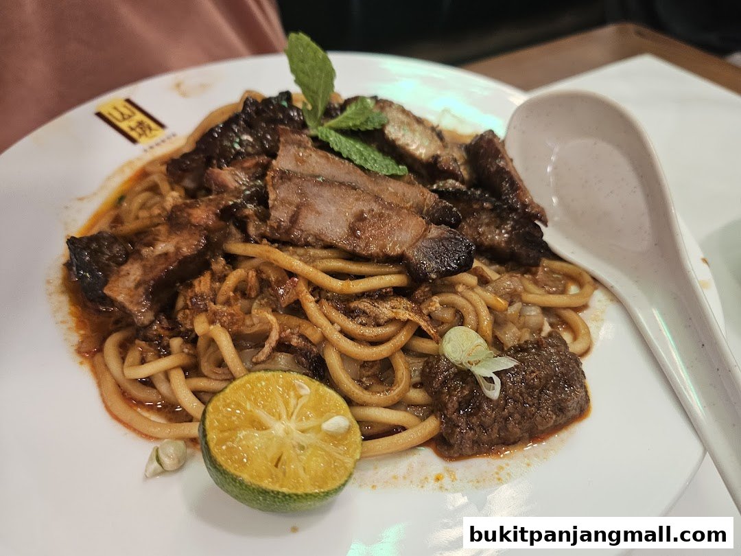A plate of Ipoh noodles with meat, lime, and mint leaves, served with a spoon.
