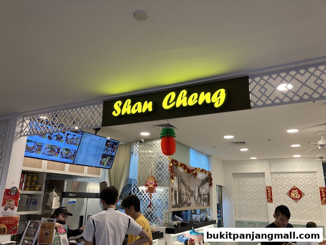 The entrance of Shan Cheng Ipoh Delicacies with a bright neon sign and digital menus.