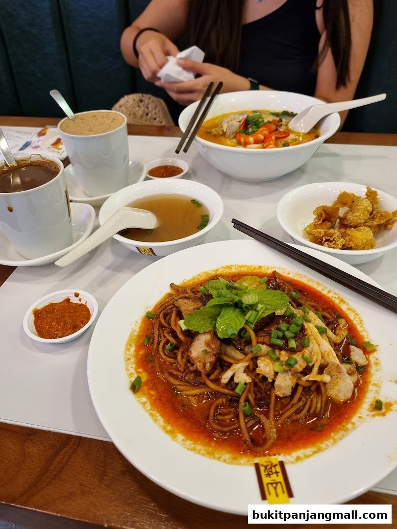 A table laden with delicious Ipoh delicacies including noodles, soup, and drinks.