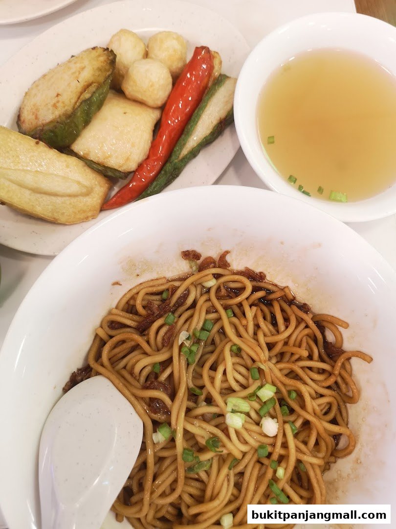 A close-up of Ipoh-style noodles with a side of fried items and a bowl of soup.