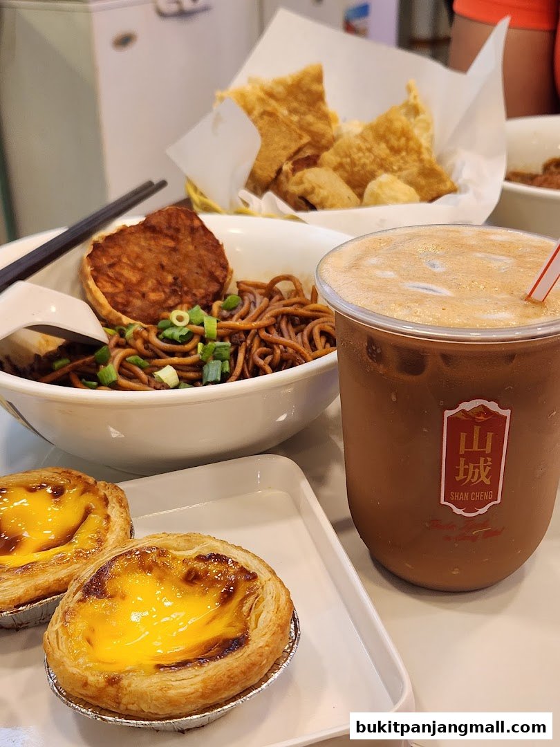 A close-up of Ipoh delicacies including noodles, fried items, egg tarts, and a drink.