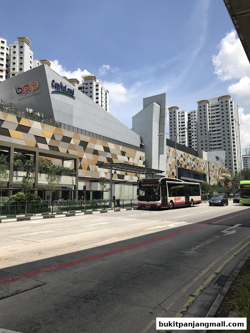 A street view of a modern shopping mall with a bus passing by.