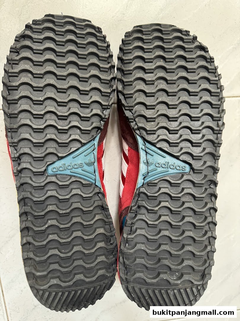 Close-up view of the soles of red and white Adidas sneakers, showing the tread pattern and branding.