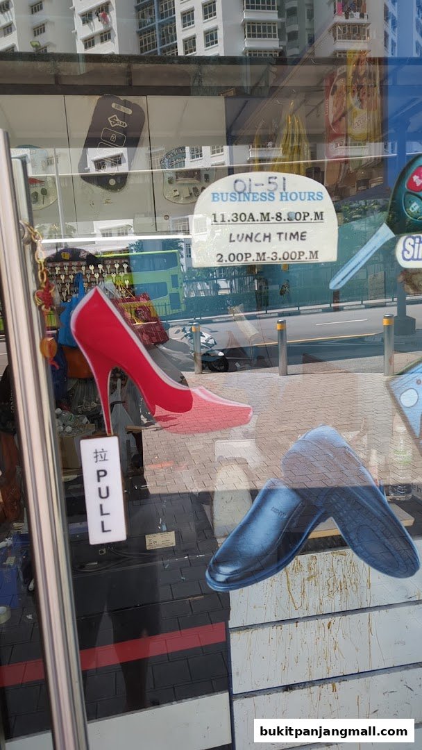 Shop window display featuring a red high heel shoe, a black dress shoe, and business hours.