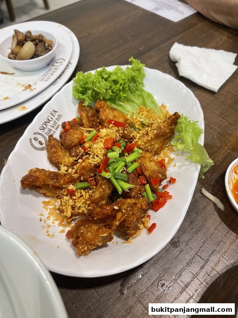 A plate of crispy fried chicken wings topped with garlic, chili, and scallions, served with lettuce.