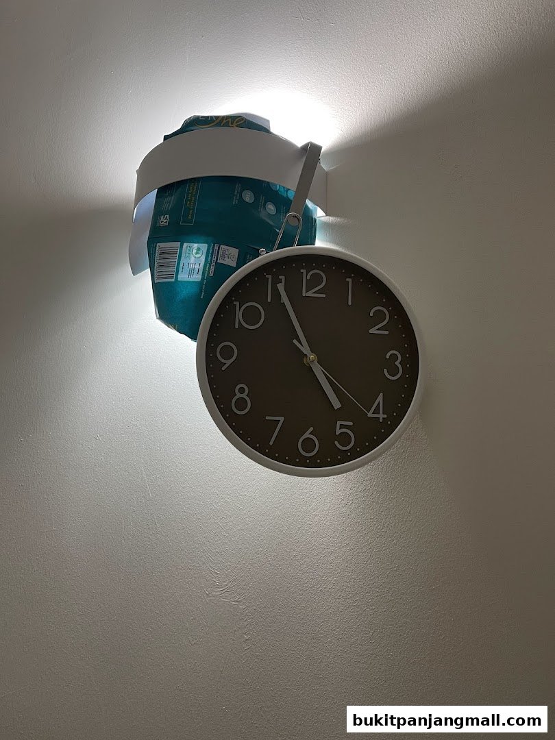 A clock hangs on a wall next to a product package illuminated by a spotlight.
