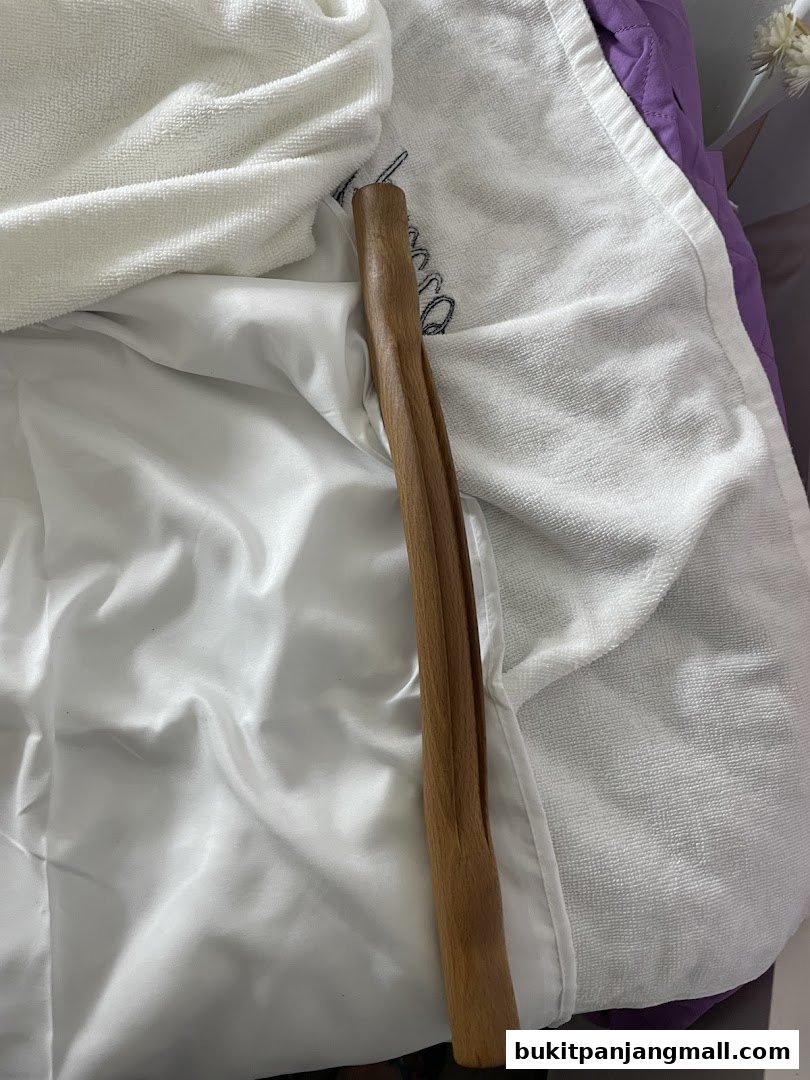 A wooden massage tool rests on white towels and a purple quilted surface.