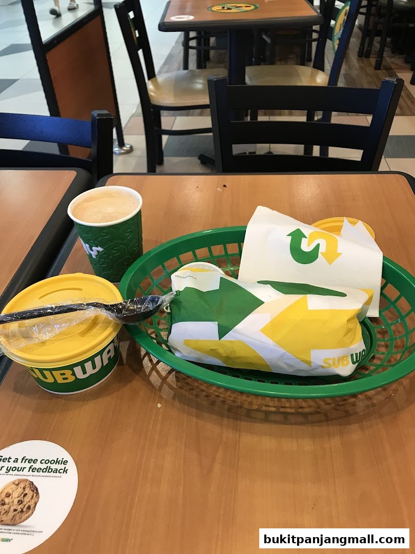 A Subway meal with a sandwich, drink, and soup on a wooden table.