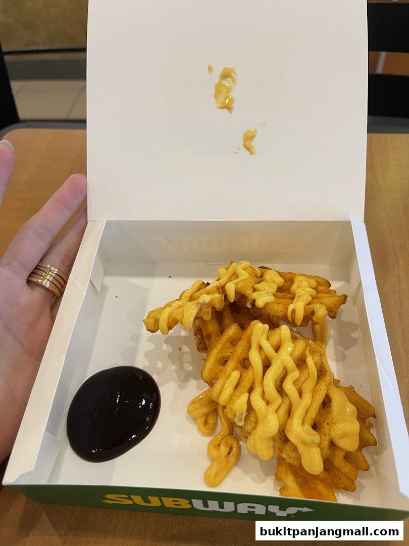 A box of waffle fries topped with cheese sauce and a side of dark sauce.