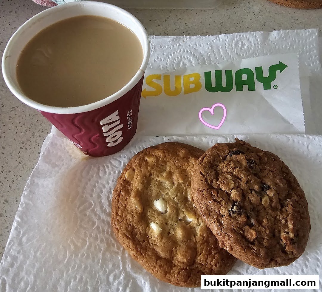 A cup of coffee and two cookies on a paper napkin with a Subway wrapper.
