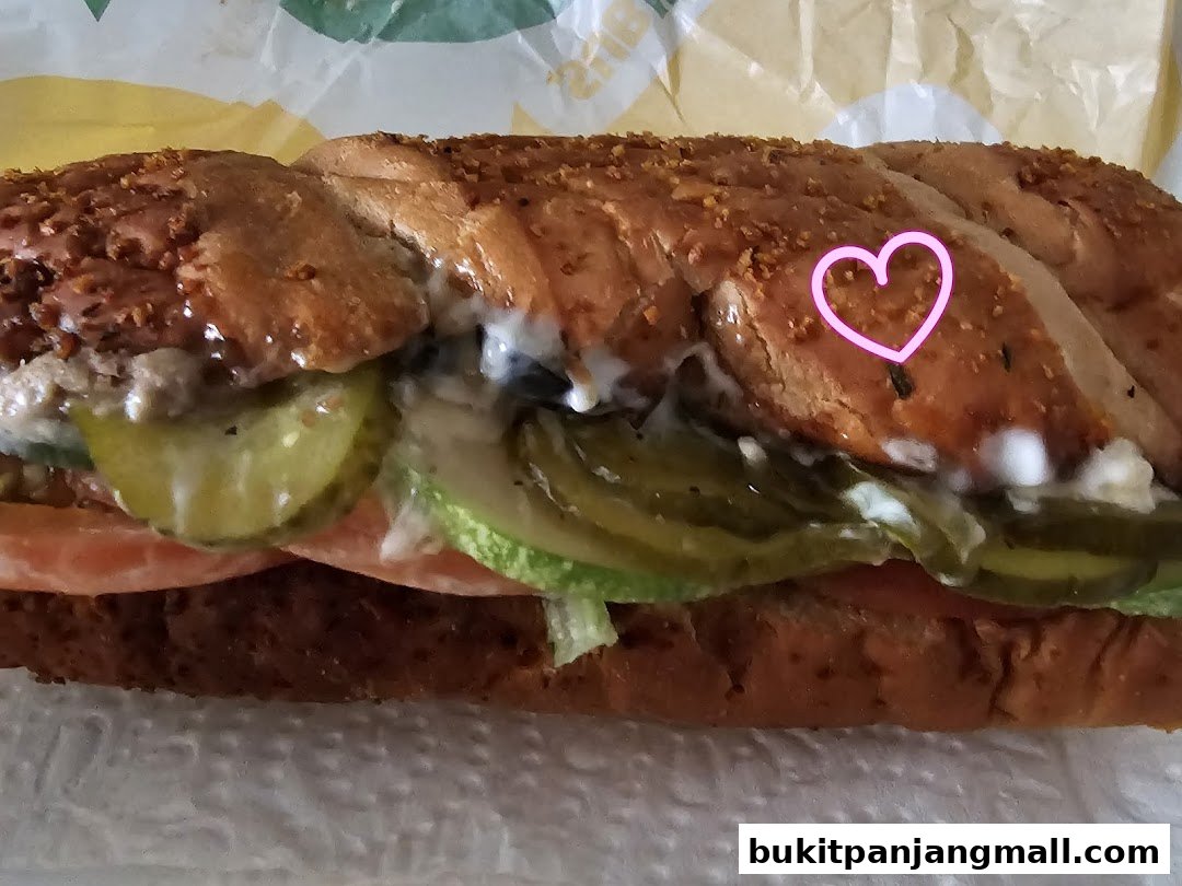 A close-up of a Subway sandwich with pickles, tomatoes, lettuce, and sauce.