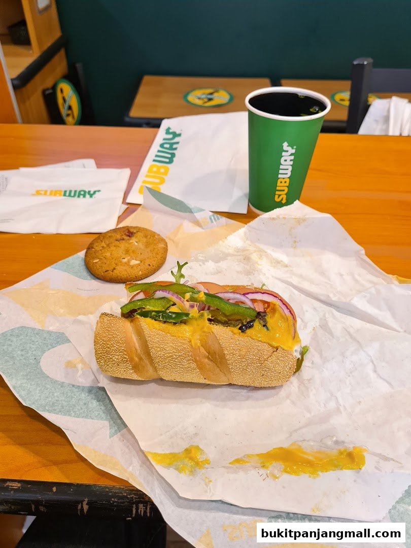 A Subway sandwich, cookie, and drink on a wooden table.