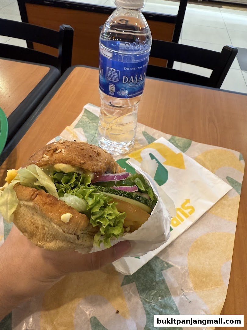 A hand holds a fresh Subway sandwich next to a bottle of Dasani water.