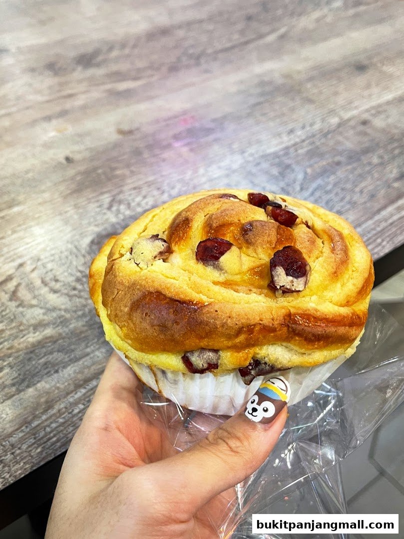 A hand holds a freshly baked, golden-brown pastry with visible cranberries.