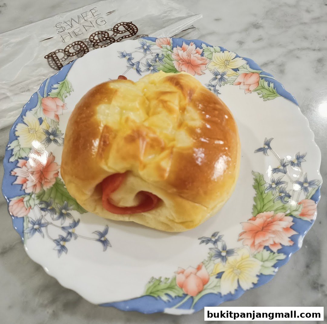 A delicious-looking bun with ham and cheese on a floral plate, with Swee Heng Bakery branding.