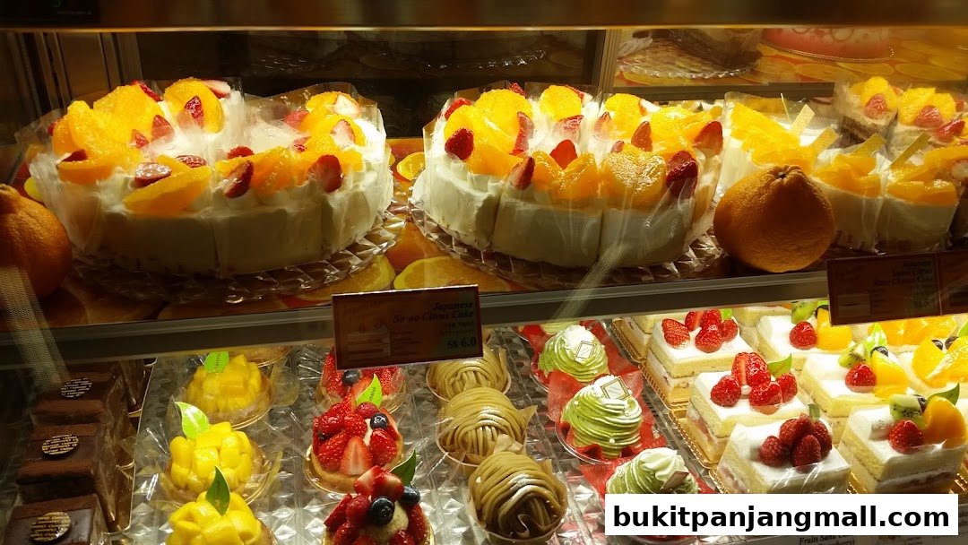 A display case filled with various cakes, including fruit-topped cakes and chocolate pastries.