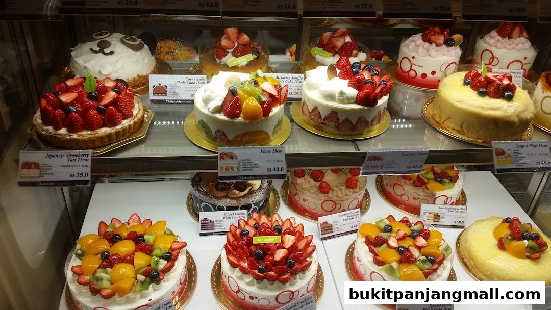 A display of various beautifully decorated cakes and tarts, featuring fresh fruits and intricate designs.