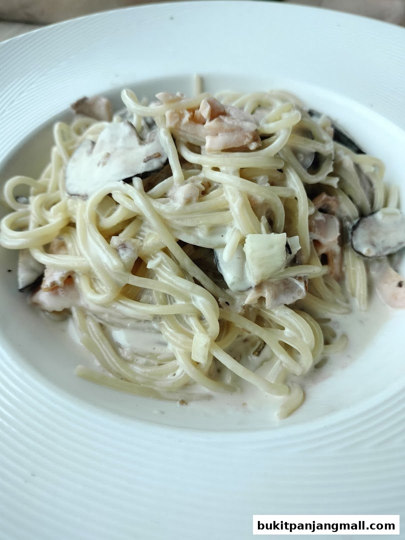 A close-up shot of creamy pasta with salmon and mushrooms served in a white bowl.
