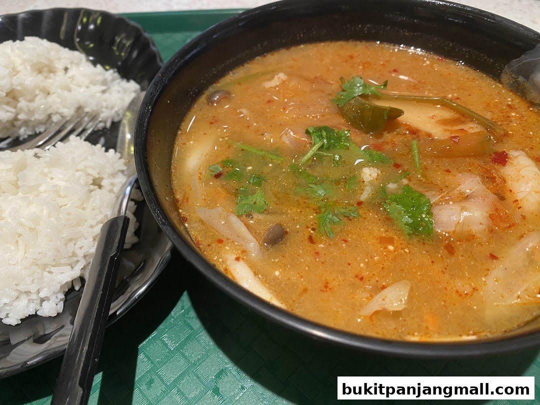 A close-up of a steaming bowl of Tom Yum soup with rice and a fork.