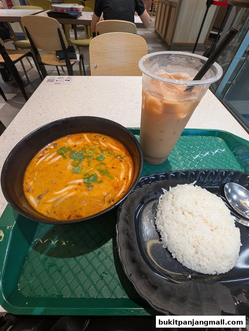 A bowl of Tom Yum soup with rice and a Thai iced tea on a tray.