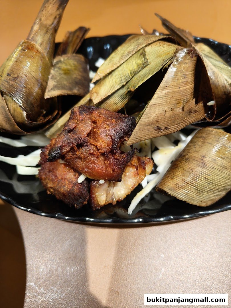 A close-up of Thai food served on a black plate, featuring meat and rice parcels wrapped in leaves.