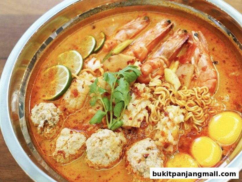 A close-up of a steaming bowl of Tom Yum soup with noodles, shrimp, meatballs, and eggs.
