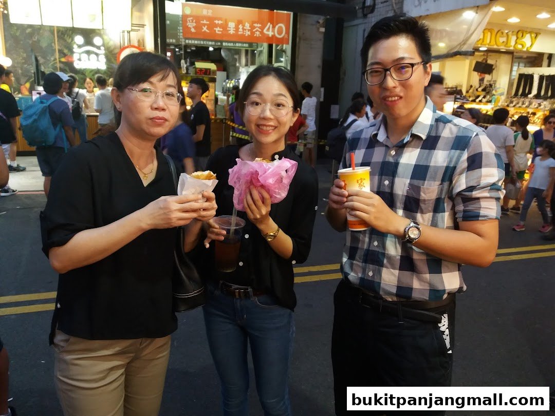 Three people smiling and holding food and drinks in an outdoor market setting.