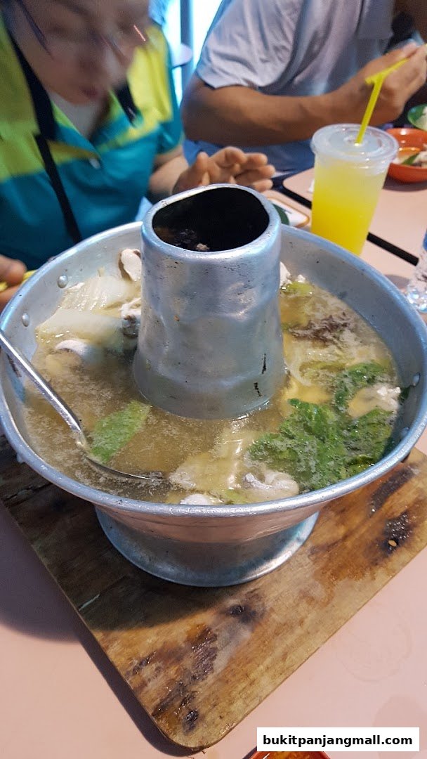 A steaming pot of seafood soup with vegetables and a person reaching for it.