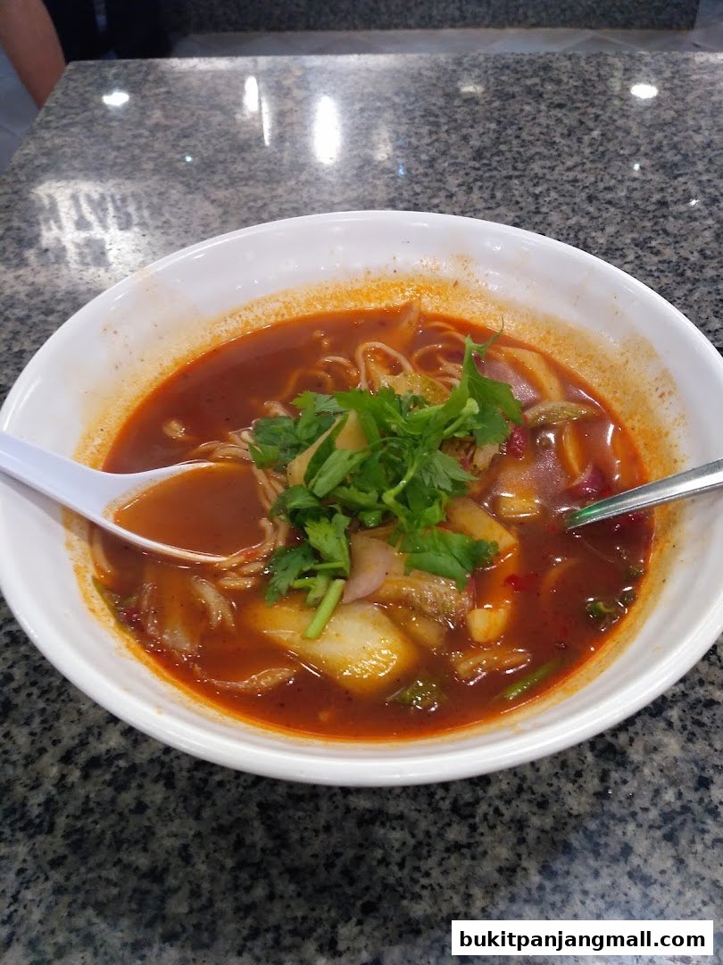 A close-up of a steaming bowl of spicy noodle soup with fresh cilantro garnish.