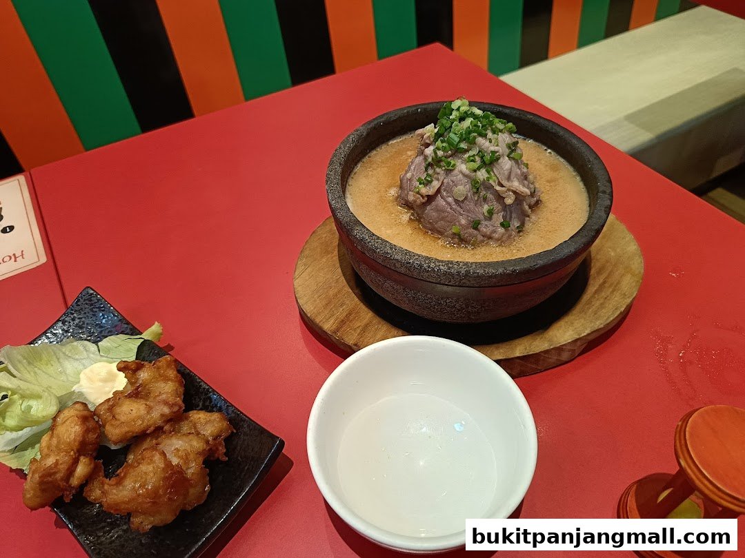 A steaming bowl of ramen with meat and chives, served with fried chicken and a side of lettuce.