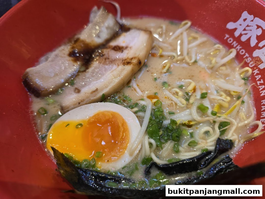 A close-up shot of a steaming bowl of Tonkotsu Kazan ramen with pork, egg, and bean sprouts.