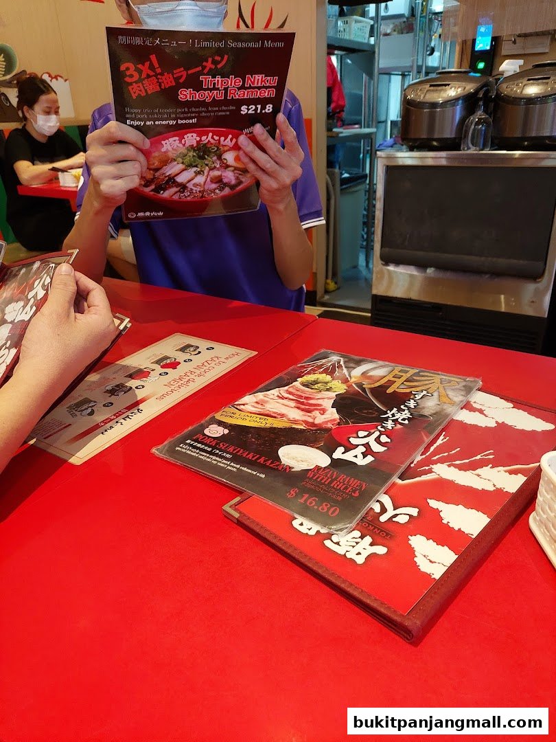 A person holding a menu for Triple Niku Shoyu Ramen at Tonkotsu Kazan.