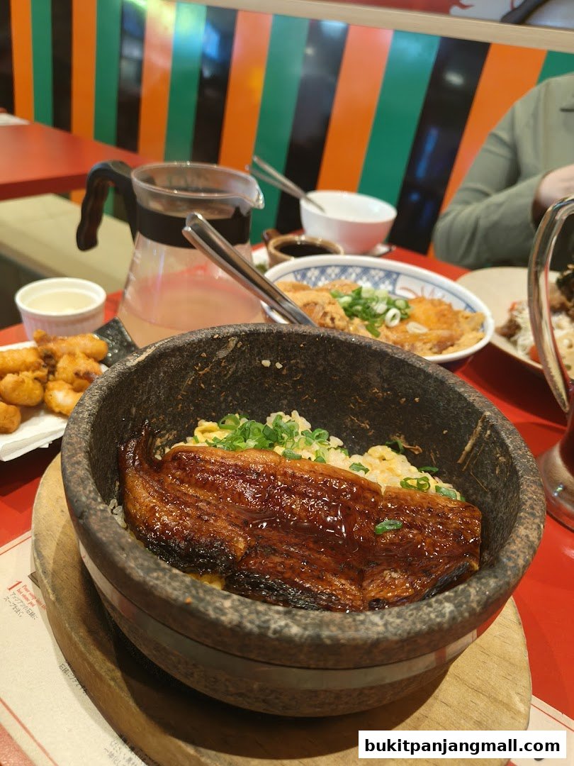 A close-up of a delicious unagi donburi served in a stone bowl with a side of fried chicken and a drink.