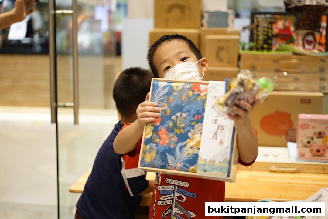 A young boy wearing a mask holds a gift box with floral patterns and snacks.