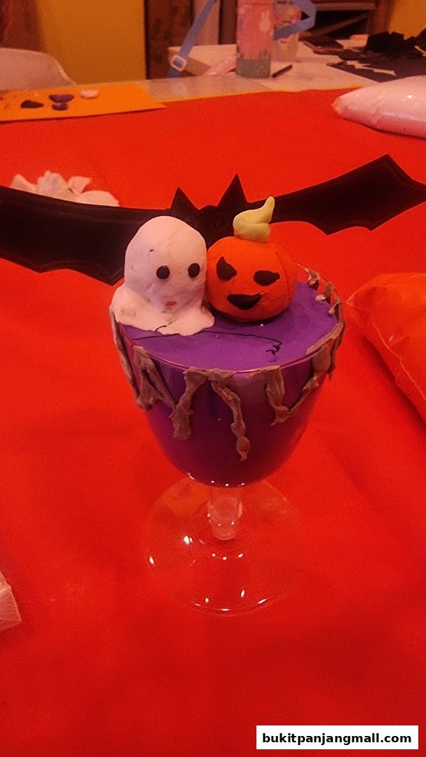 A Halloween-themed craft project featuring a ghost and pumpkin in a purple cup.