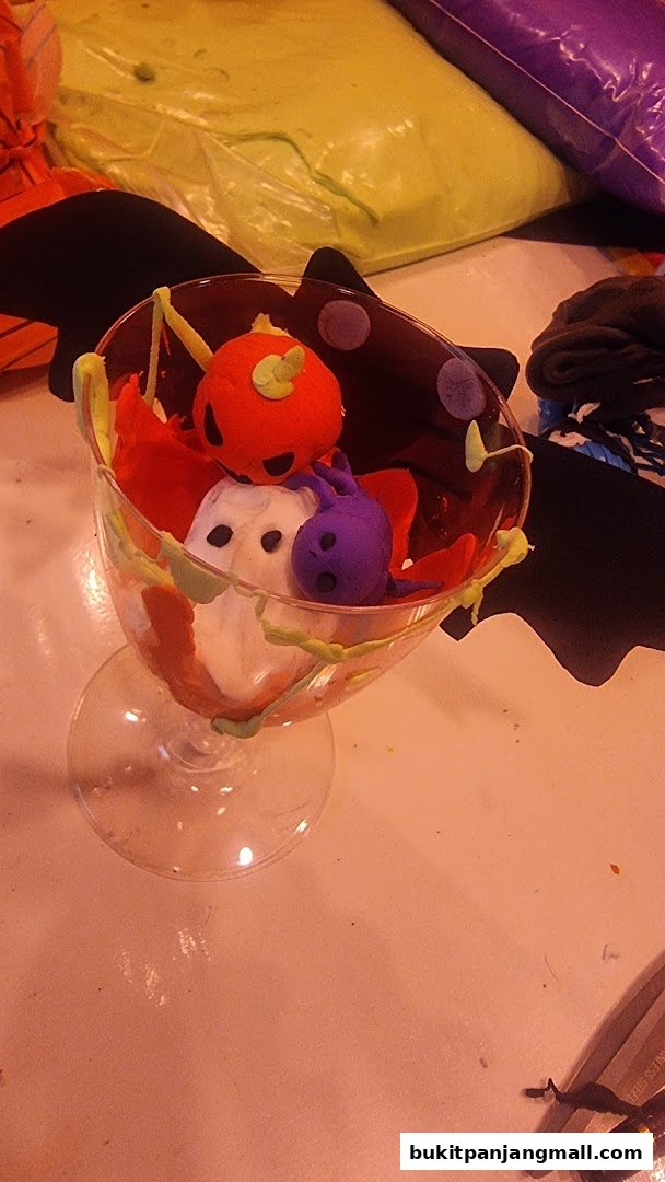 A glass filled with Halloween-themed clay figures, including a pumpkin, ghosts, and a purple creature.