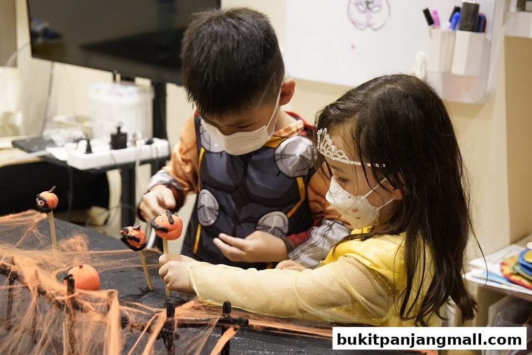 Two children in Halloween costumes and masks are decorating pumpkin cake pops.