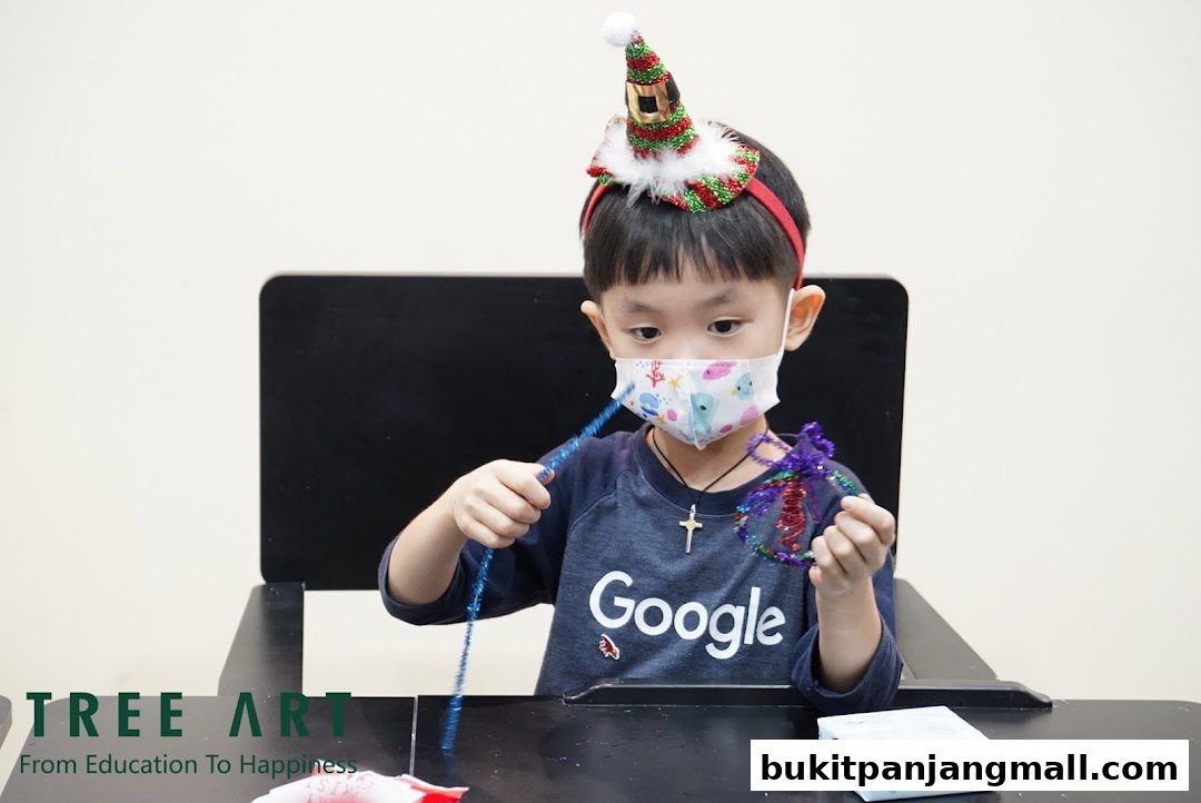 A young boy wearing a festive hat and mask is crafting a sparkly ornament.