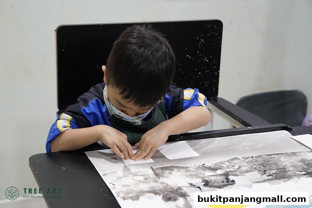 A young child wearing a mask and apron concentrates on an art project at a table.