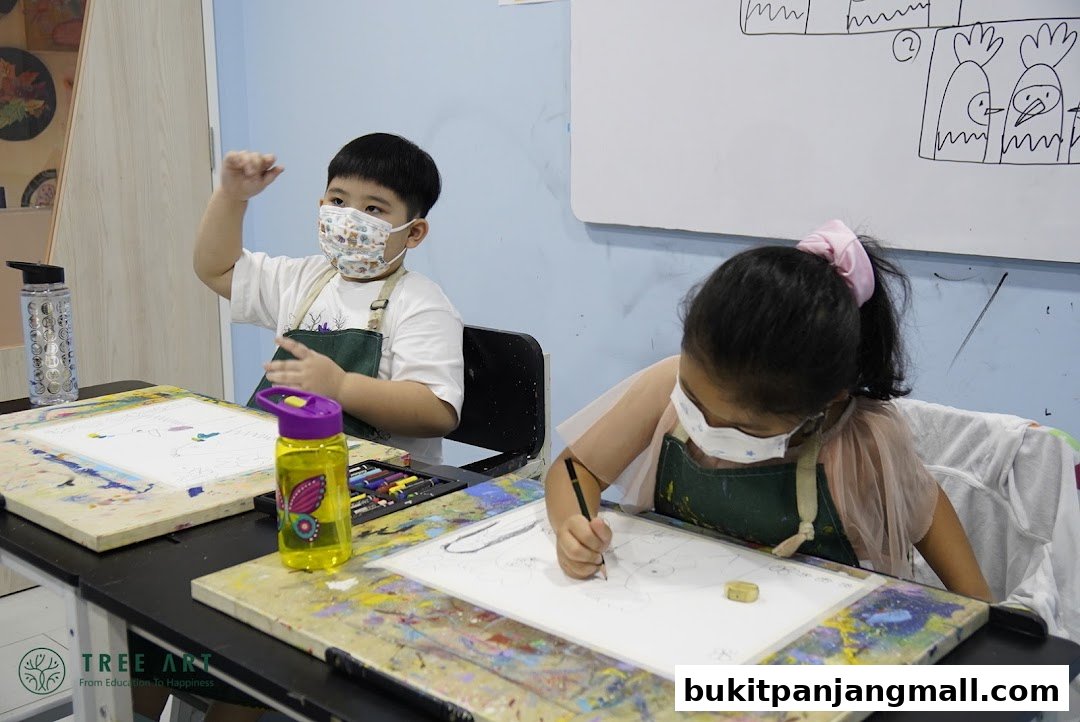 Two children wearing masks and aprons are drawing at tables in an art class.