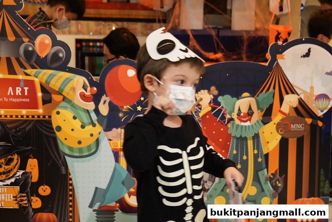 A child in a skeleton costume poses in front of a Halloween-themed circus backdrop.