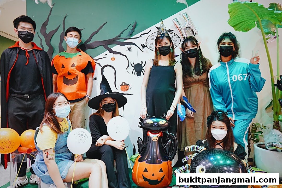 A group of people in Halloween costumes pose with festive decorations and balloons.