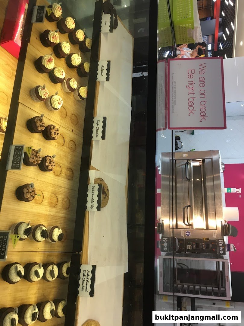 A display case filled with cupcakes and cookies, with a 'Be right back' sign visible.