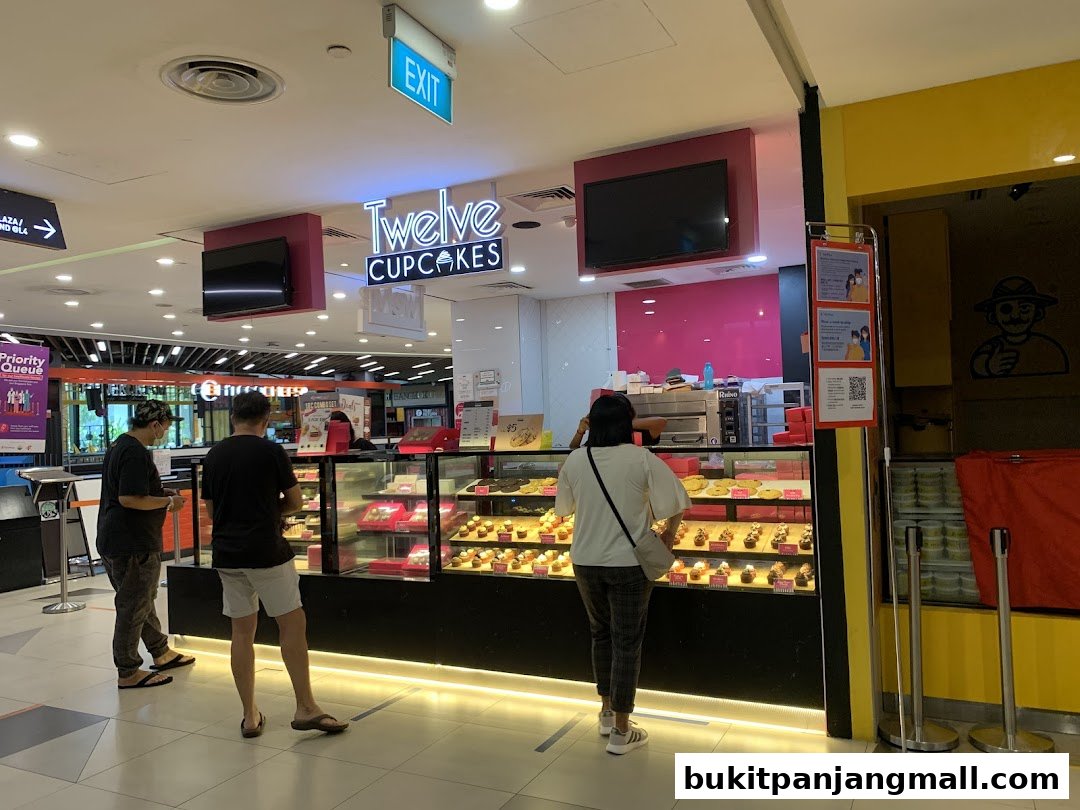 Customers browse cupcakes at a brightly lit Twelve Cupcakes store with a display case full of treats.