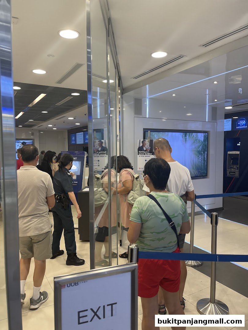 People queuing inside a UOB bank branch with an exit sign in the foreground.