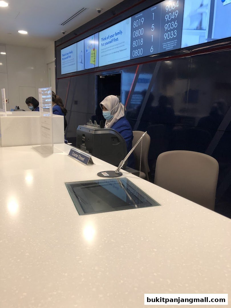 Bank counter with staff serving customers and a digital display showing queue numbers.