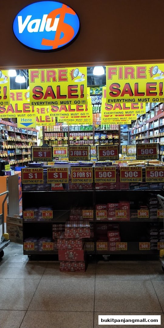 The entrance of a Valu store with a large "FIRE SALE! EVERYTHING MUST GO!!!" banner and various product displays.