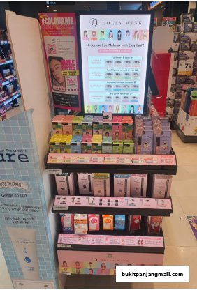 A display stand featuring Dolly Wink eye makeup products and other beauty items.