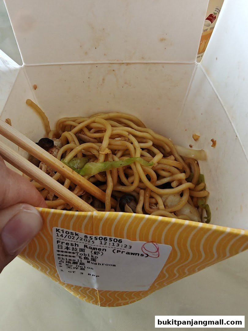 A person is holding chopsticks in a takeaway box filled with noodles and vegetables.
