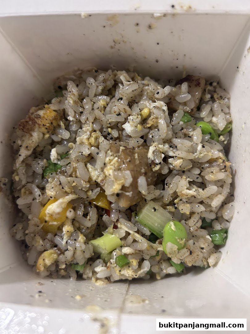 A close-up shot of a takeaway box filled with savory fried rice, featuring edamame and spring onions.